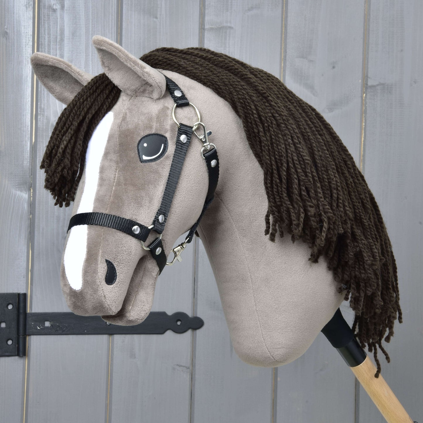 The Hobby Horse LarDen Guccini with Black Halter features a plush Holsteiner stallion with gray face, white nose stripe, long brown yarn mane, and wooden stick—ideal for aspiring equestrian sport fans.