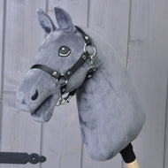 Zbuduj swojego konia, personalizowany Hobby Horse z ciemnoszarą pluszową głową, czarną uzdą i drewnianym kijem, na tle pionowych drewnianych desek.