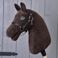 Zbuduj swojego konia, pluszowa personalizowana głowa Hobby Horse w ciemnobrązowym kolorze, z czarnym ogłowiem i wodzami oraz efektowną białą grzywą, przymocowana do drewnianego kija i pokazana przed szarymi drewnianymi panelami.