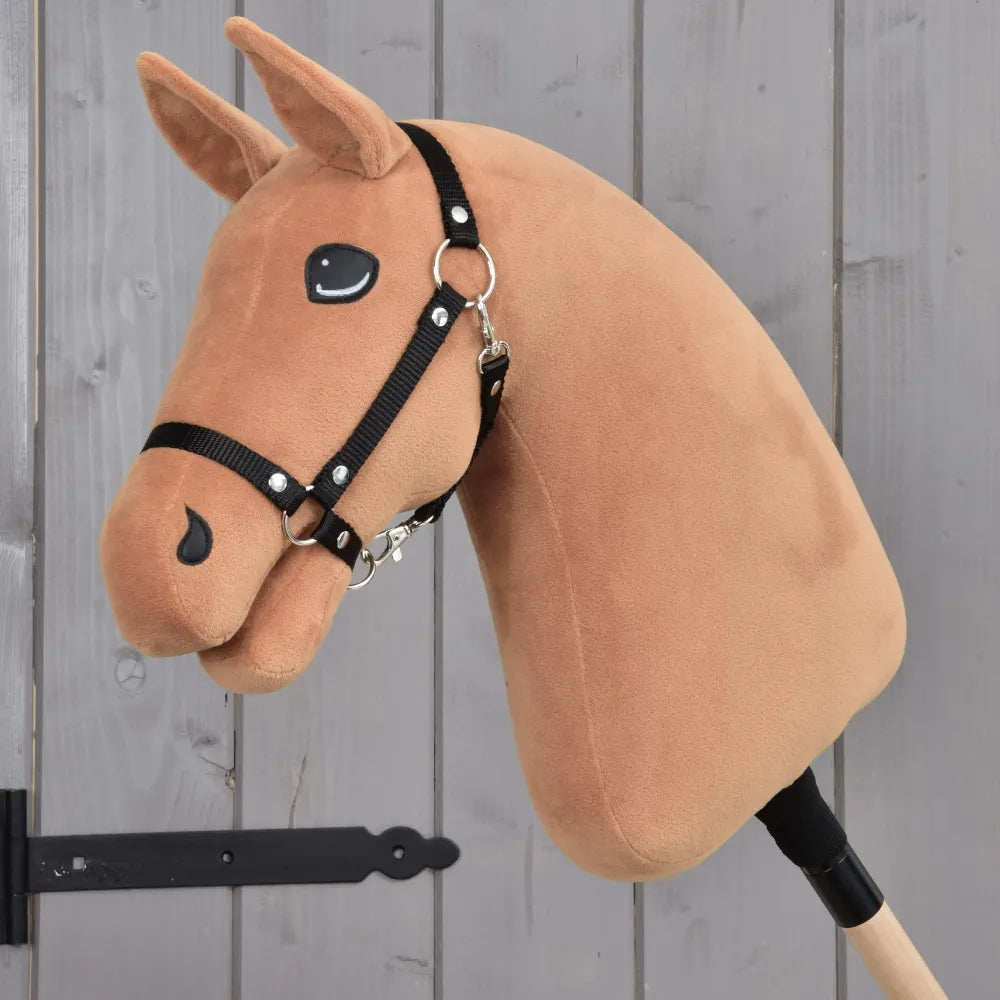 The Build your horse hobby horse by related_to_12441055625556 features a chestnut brown plush custom head with a black bridle, mounted on a stick and displayed against a gray wooden background with a visible black metal hinge on the left.