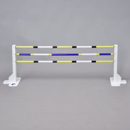 A white horse jumps the Hobby Horse LarDen Jump 50 cm / 20 inch with extra yellow, white, blue, and black poles against a gray background. Ideal for indoor or outdoor Hobby Horsing activities.