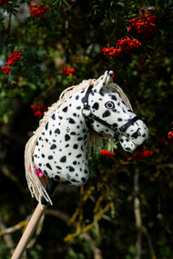 Lifestyle photo: the Hobby Horse Lord Valentine with Black Halter by Hobby Horse LarDen in front of a rowan tree with clusters of red berries - white plush head with black leopard spots, cream yarn mane, black halter with silver fittings.