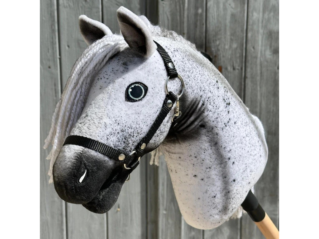 Zbliżenie na Hobby Horse Naivy z czarnym kantarem - rozmiar S od Hobby Horse LarDen, realistycznego szarego ogiera z białą grzywą i czarnym kantarem, osadzonego na kiju na rustykalnym drewnianym tle.