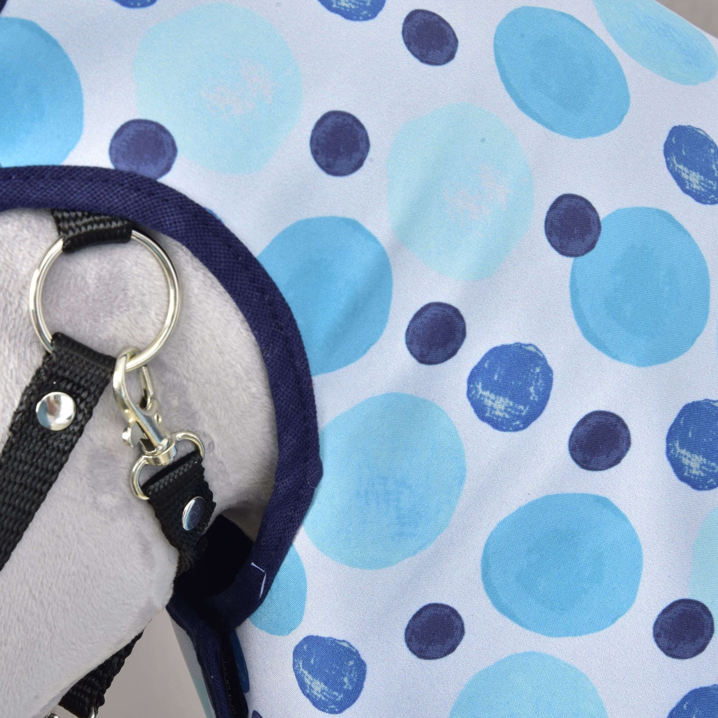 A close-up of Raincoat Bubbles by Hobby Horse LarDen shows blue and navy polka dot fabric with a metal ring and clip—an ideal all-weather hobby horse accessory, displayed on a light gray surface.