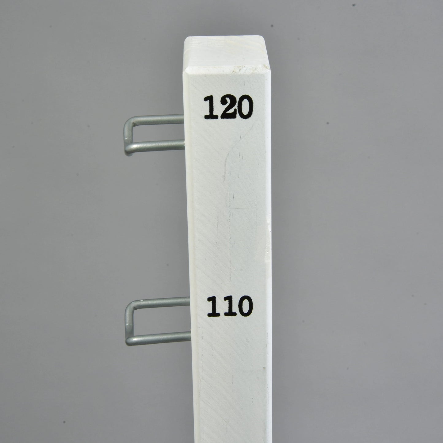 A white vertical pole from the Hobby Horse LarDen Jump 120 cm / 47 inch set, featuring black numbers 120 and 110 and two metal hooks on the side, stands against a plain gray background.