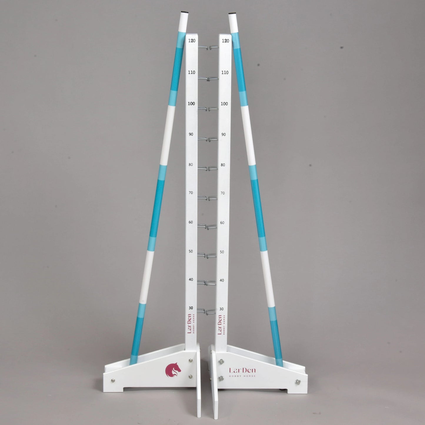 The Hobby Horse LarDen Jump 120 cm / 47 inch is a white and blue adjustable pet jump stand with two poles, white bases, and a central height scale from 10 to 180 cm. Ideal for cavaletti training. Shown against a plain gray background.
