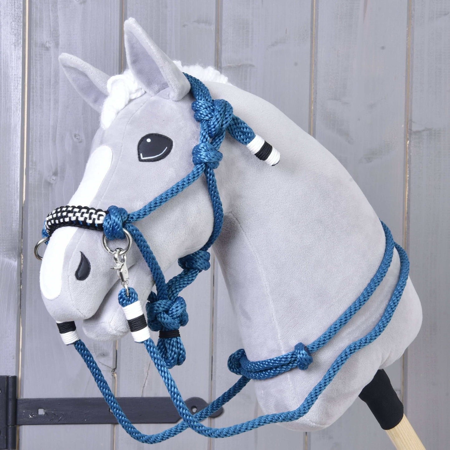 Zestaw sznurkowy Chess od Hobby Horse LarDen na pluszowym Hobby Horse z szarą głową, białą strzałką oraz niebieskim kantarem, wodzami i cordeo z czarno-białymi akcentami, pokazany na tle drewnianej ściany.