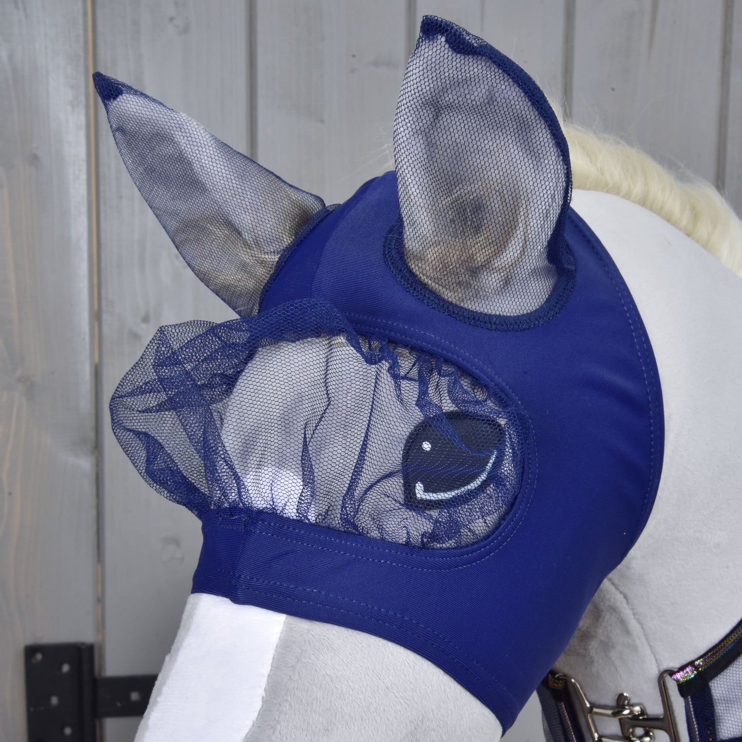 Biały koń nosi granatowy Zestaw Fly Combo od Hobby Horse LarDen z siatkowymi osłonami uszu i oczu. Idealny do stylu Hobby Horsing, ta maska chroni oczy i uszy konia przed owadami.