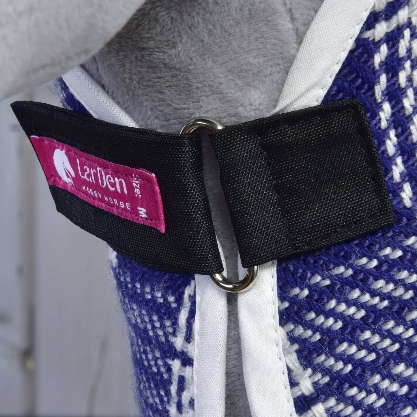 Close-up of a fabric halter strap with a metal ring, featuring a pink label reading Hobby Horse LarDen on the Set Harmony Victory stable blanket, made from textured blue and white patterned material.