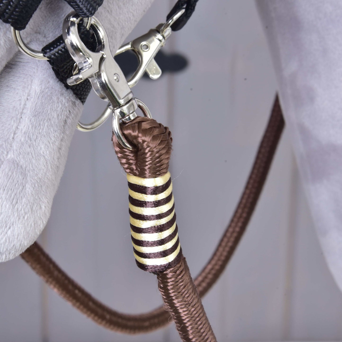 Zbliżenie metalowego klipsa mocującego brązową linę polipropylenową ze złotym i czarnym ozdobnym oplotem do szarego materiału, część Wodzy Vivaldi od Hobby Horse LarDen.