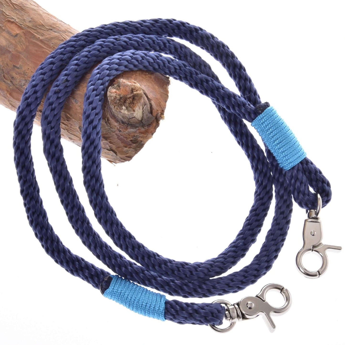 The Rope set Dark Blue by Hobby Horse LarDen features a coiled dark blue leash with metal clasps at both ends, each wrapped with bright blue thread, and is displayed on a light brown wooden branch—a stylish riding accessory.