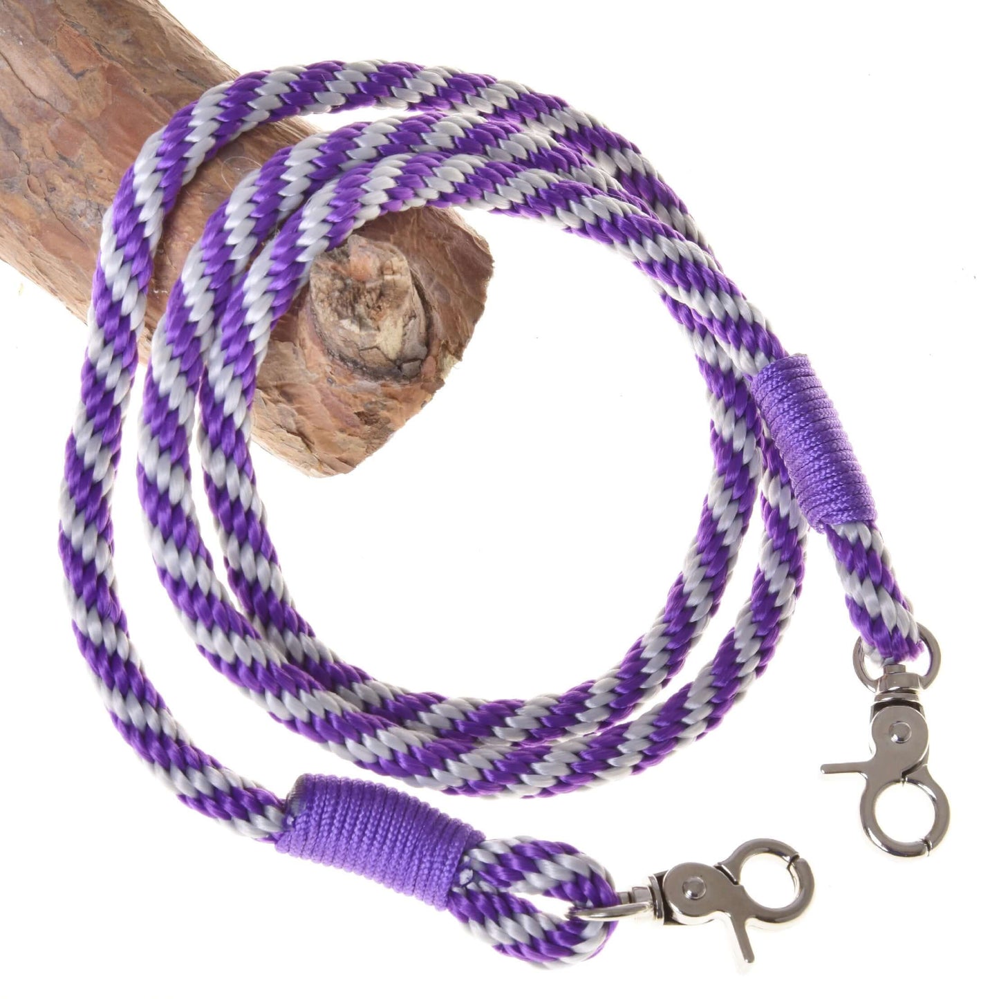 The Hobby Horse LarDen "Hobby Horse - Reins lila stripe" is a coiled, purple-and-white striped rope leash with metal clasps at both ends, ideal for handmade hobby horse reins and shown here displayed on a wooden branch.